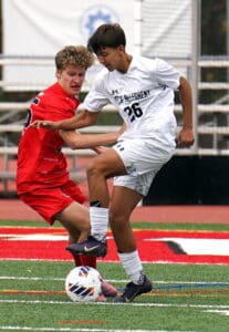 Two soccer players compete for the ball on a field, wearing red and white uniforms.