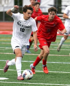 Two soccer players compete for the ball during a high school match on a green field.