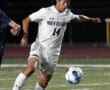 Soccer player in white uniform kicking ball on field at night match.