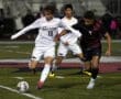 Soccer players compete fiercely for the ball during a nighttime match on a grassy field.