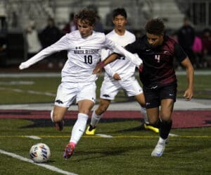 Soccer players compete fiercely for the ball during a nighttime match on a grassy field.