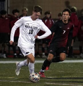 Two high school soccer players compete for ball possession on a field during a night match.