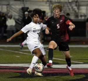 Two soccer players in action during a nighttime match, one in white and the other in black and red.