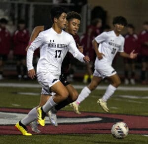 Soccer players from North Allegheny in action during a night match, competing fiercely for ball possession.