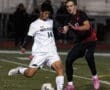 Two soccer players competing for the ball during a night match on a grassy field.