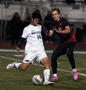 Two soccer players competing for the ball during a night match on a grassy field.