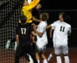 Soccer goalie in yellow leaps to catch the ball, surrounded by players in a nighttime match.