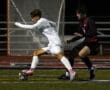 Two soccer players competing for the ball near the goal during a nighttime match on the field.