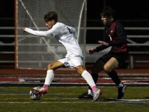 Two soccer players competing for the ball near the goal during a nighttime match on the field.