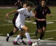 Soccer players compete for the ball during a night match on a grass field.