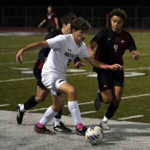 Soccer players compete for the ball during a night match on a grass field.