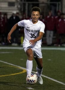 Soccer player in white uniform dribbles ball on field during match at night, focused on gameplay.