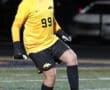 Soccer goalie in yellow jersey and gloves controls the ball during a night game on turf field.