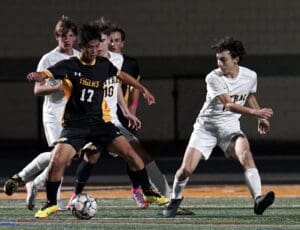High school soccer match action shot, players competing for the ball under stadium lights.