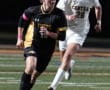 Soccer players in action on the field under stadium lights, one in black and one in white, chasing a soccer ball.