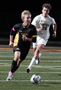 Soccer players in action on the field under stadium lights, one in black and one in white, chasing a soccer ball.