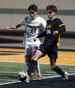 Two high school soccer players in action, wearing white and black uniforms, competing for the ball on the field.