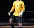 Young soccer goalkeeper in yellow jersey prepares to kick ball on sports field at night.