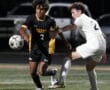 Two soccer players compete for the ball during a night match on a grassy field.