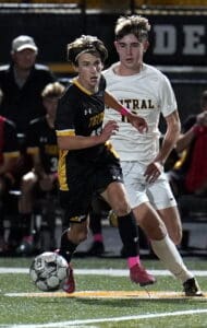 Two soccer players in a match, one in a black Tigers uniform, dribbling the ball on a lit field.