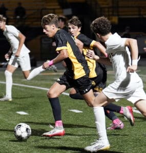 Soccer match action: players in yellow and black vs. white on field, competing for the ball at night game.