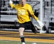 Goalkeeper in yellow jersey kicking soccer ball on field during a game.