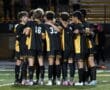 Soccer team huddle on field in yellow and black uniforms, showing teamwork and unity at night match.