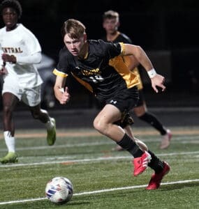 Soccer player in black and yellow sprinting towards the ball during a night match on a field.