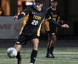 Soccer player in a black and yellow Tigers uniform kicks a ball during a night game on the field.
