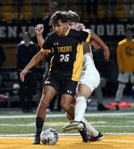 Soccer player in black and yellow jersey controls ball against defender on field during night match.