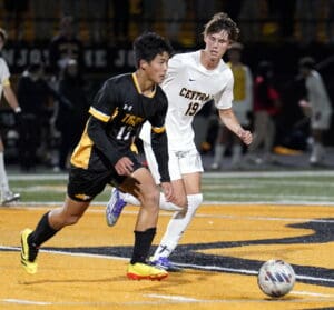 Two soccer players in action on a field during a night match, focused on the ball.