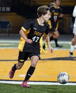Soccer player in black and yellow jersey dribbles the ball during a night game on a turf field.