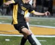 Soccer player in black uniform kicking ball during night game on turf field.