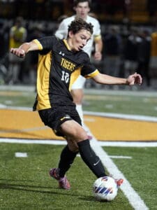Soccer player in black uniform kicking ball during night game on turf field.