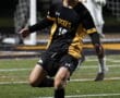 Soccer player in black and yellow Tigers uniform focuses on ball during game on green field.