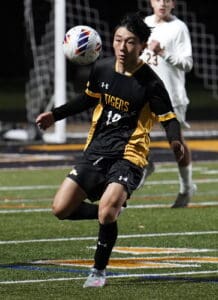 Soccer player in black and yellow Tigers uniform focuses on ball during game on green field.