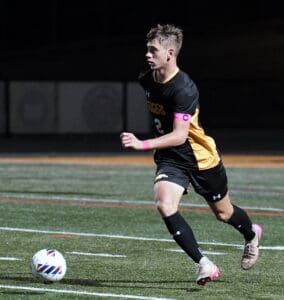 Soccer player in action on the field, wearing a black and yellow kit, sprinting towards the ball at night.