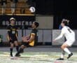Soccer players competing under stadium lights, focusing on a high ball during a nighttime match.