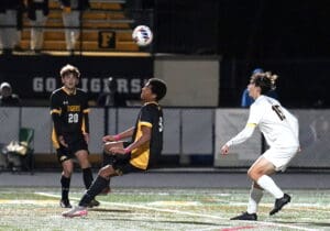 Soccer players competing under stadium lights, focusing on a high ball during a nighttime match.