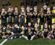 Soccer team celebrating a win on the field wearing black and yellow Tigers jerseys at night.