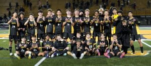 Soccer team celebrating a win on the field wearing black and yellow Tigers jerseys at night.