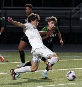 Soccer players in action during a match on a green field at night, focused on kicking the ball.
