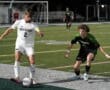 Two soccer players in action during a nighttime match, focused on the ball near the sideline.