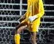 Soccer goalie in yellow kit controls ball on field during night match.
