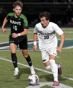 Two soccer players in black and white uniforms compete for the ball during a night match on the field.