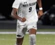 Soccer player in white North Allegheny kit dribbling a ball on the field during a match at night.