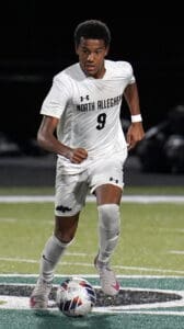 Soccer player in white North Allegheny kit dribbling a ball on the field during a match at night.