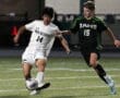Two high school soccer players compete for the ball during a night match on the field.