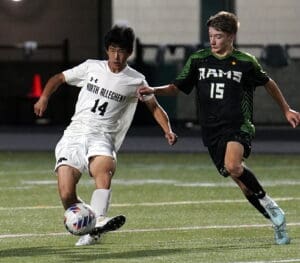 Two high school soccer players compete for the ball during a night match on the field.