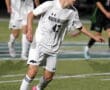 Soccer player in white North Allegheny uniform dribbling a ball on the field during a game.